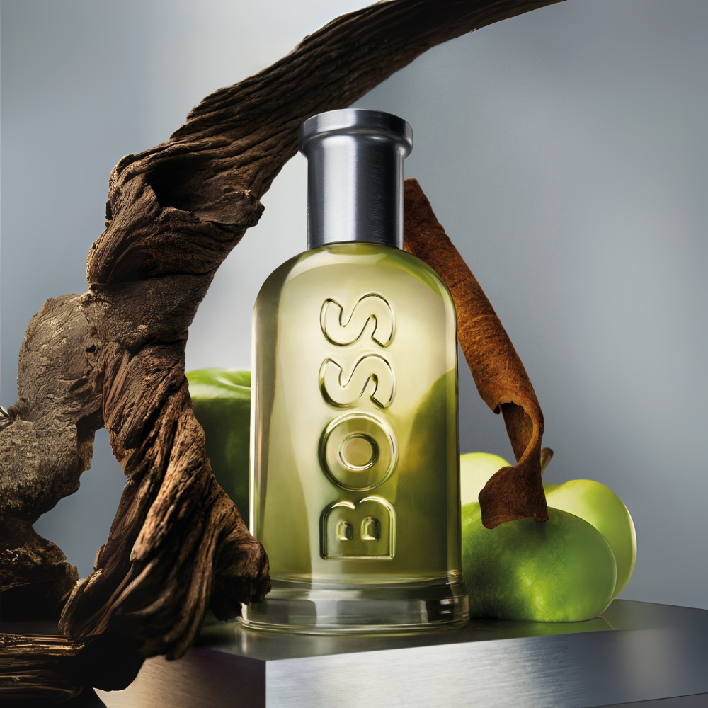 BOSS perfume bottle with green apples and wooden elements on a gray background